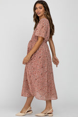 woman wearing a pink floral maternity dress with short sleeves, showing her baby bump and a pleated skirt