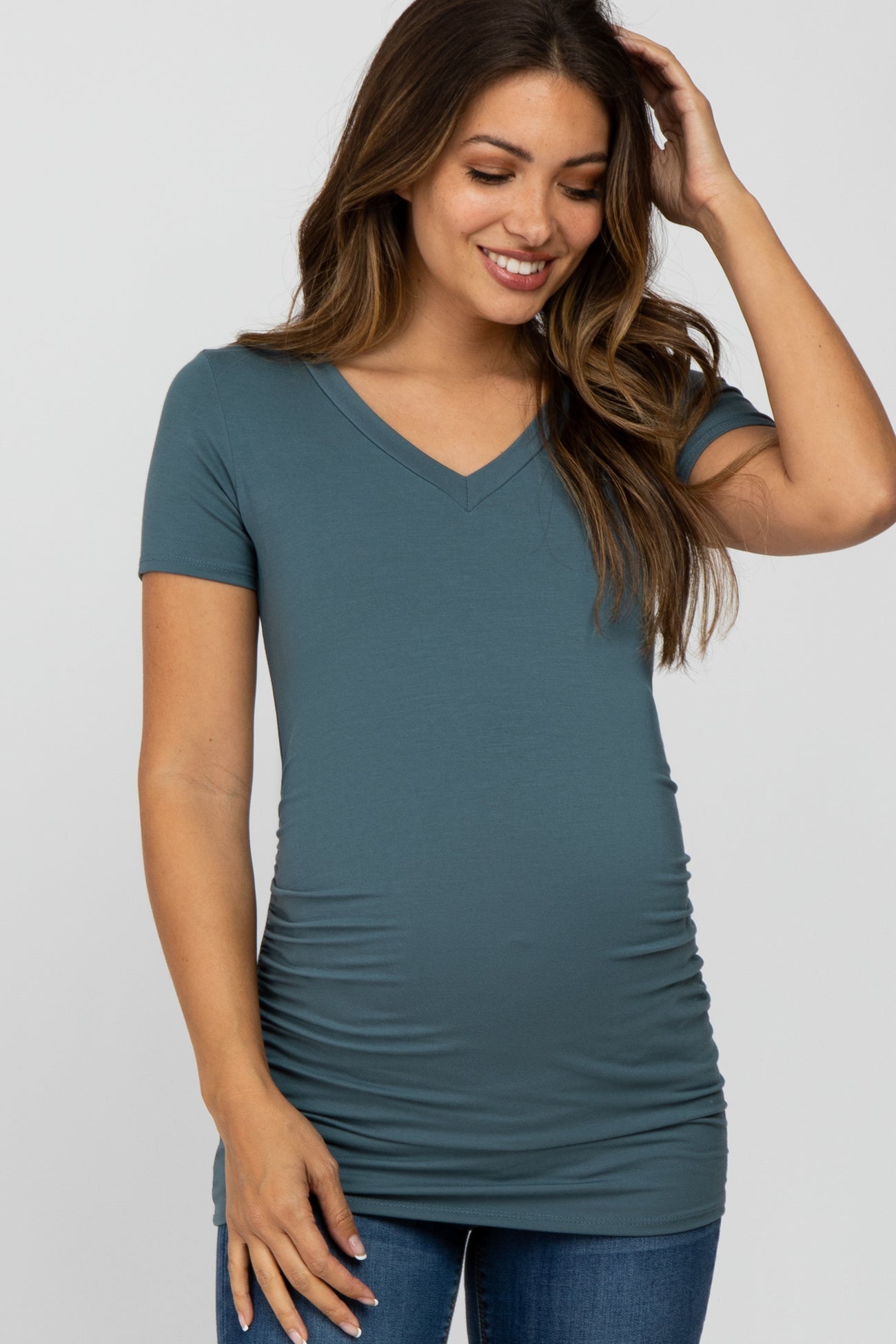 woman wearing a teal v-neck maternity top with ruching, showing her baby bump, paired with jeans