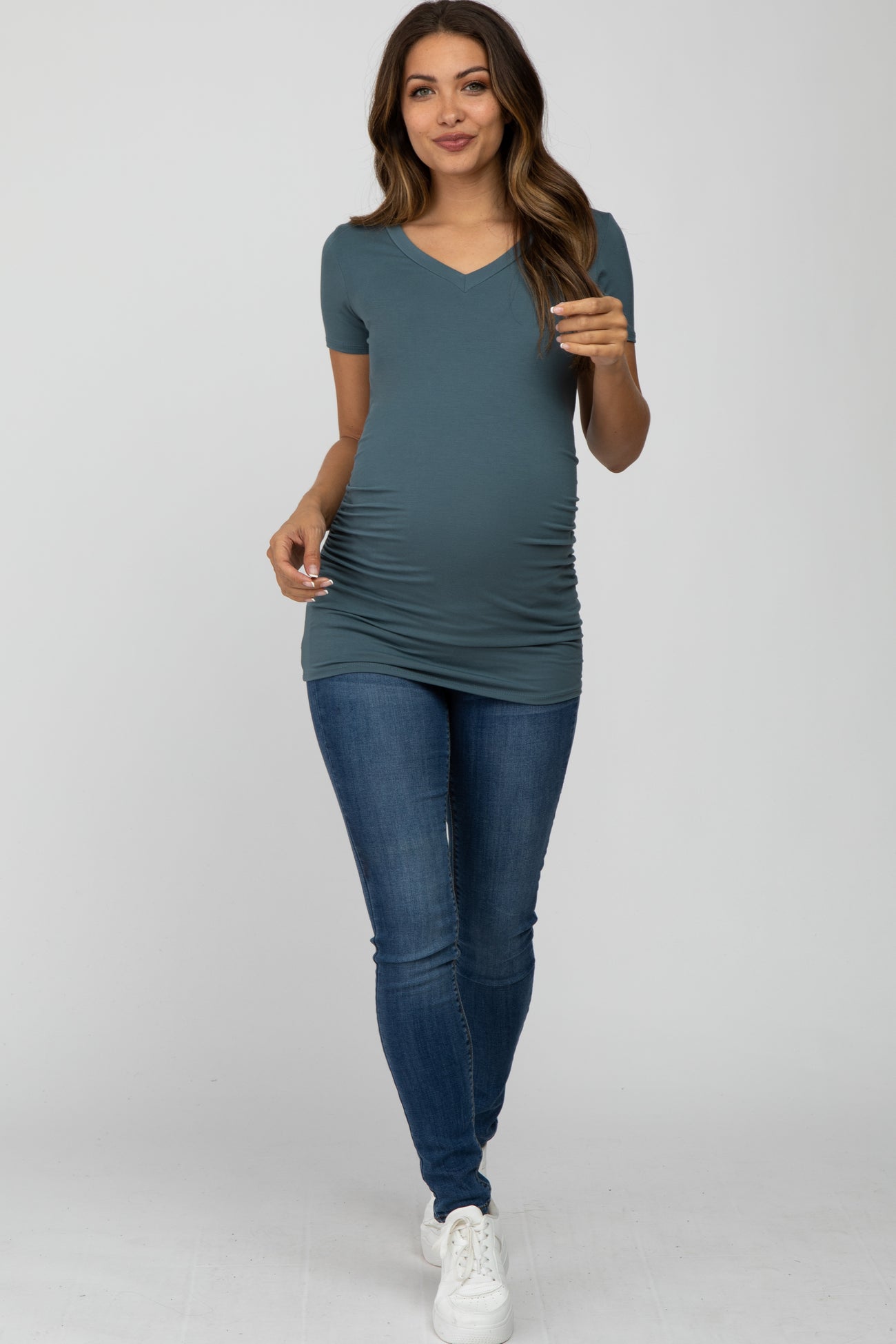 woman wearing a teal short sleeve maternity top that accentuates her baby bump and paired with skinny jeans