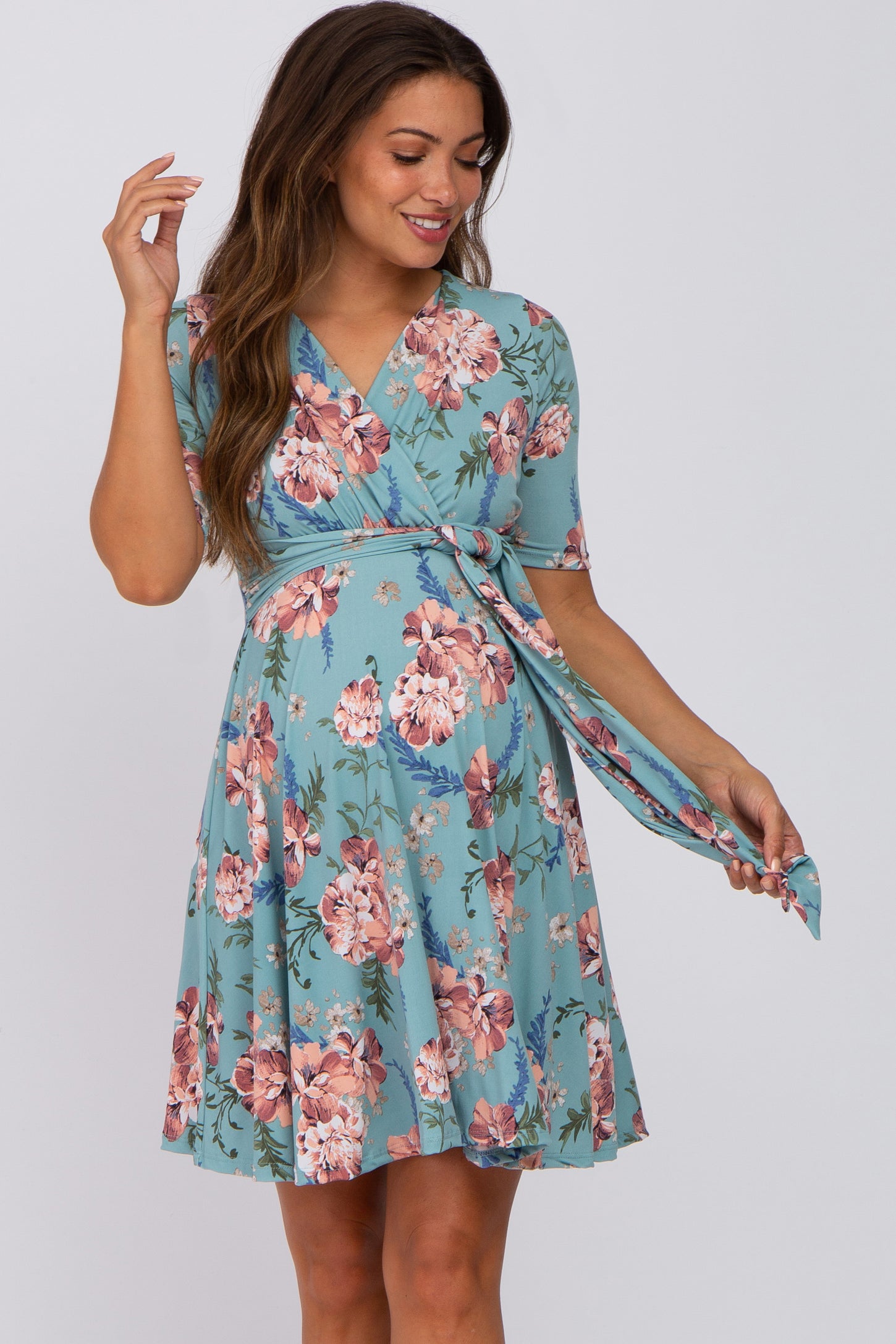 woman wearing a light blue floral print maternity wrap dress with short sleeves and a tied waist, highlighting her baby bump