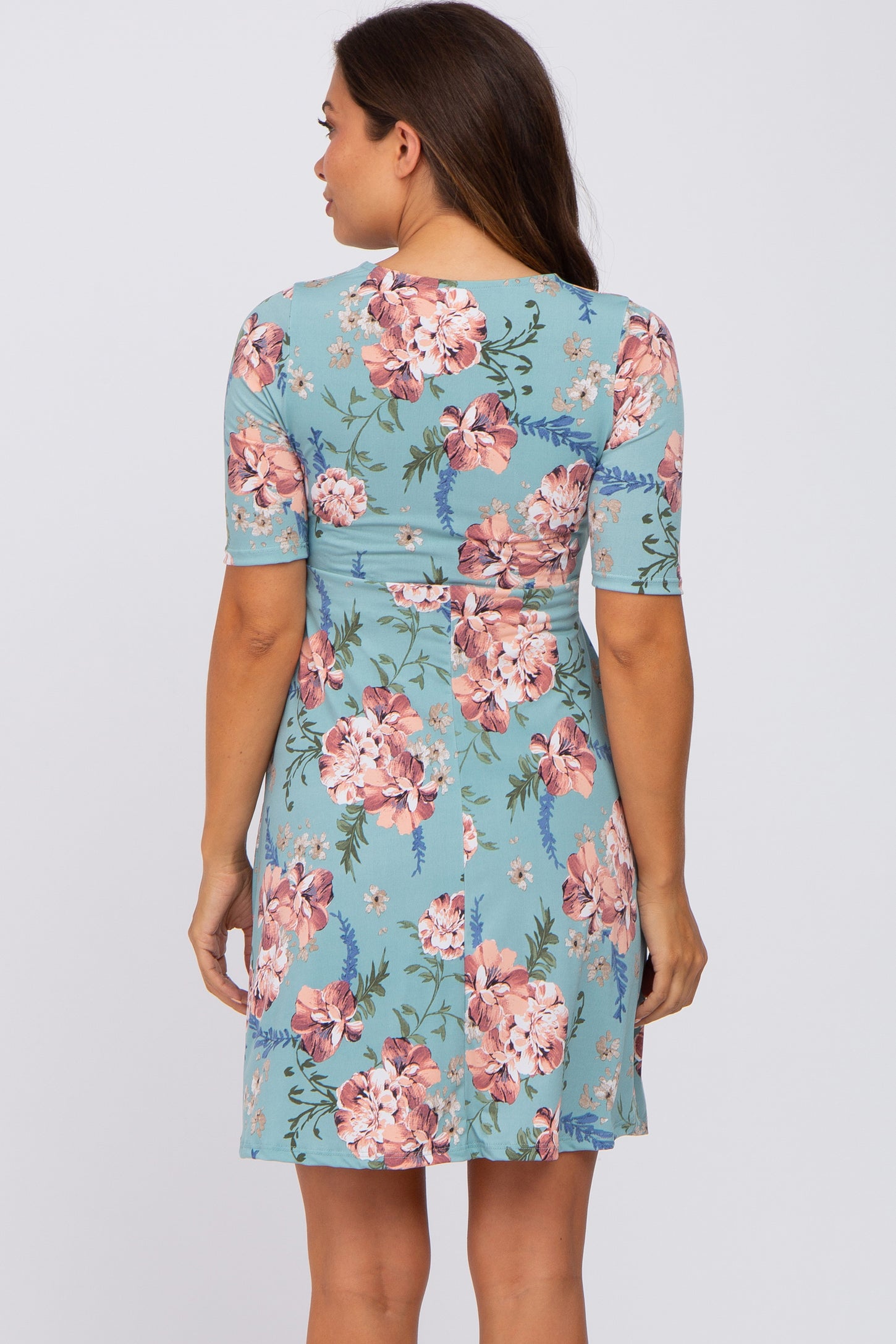 Back view of a woman wearing a light blue short sleeve maternity dress with a pink floral print pattern
