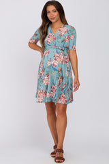 woman wearing a light blue floral maternity dress with short sleeves and a wrap design, standing confidently with one hand on her hip