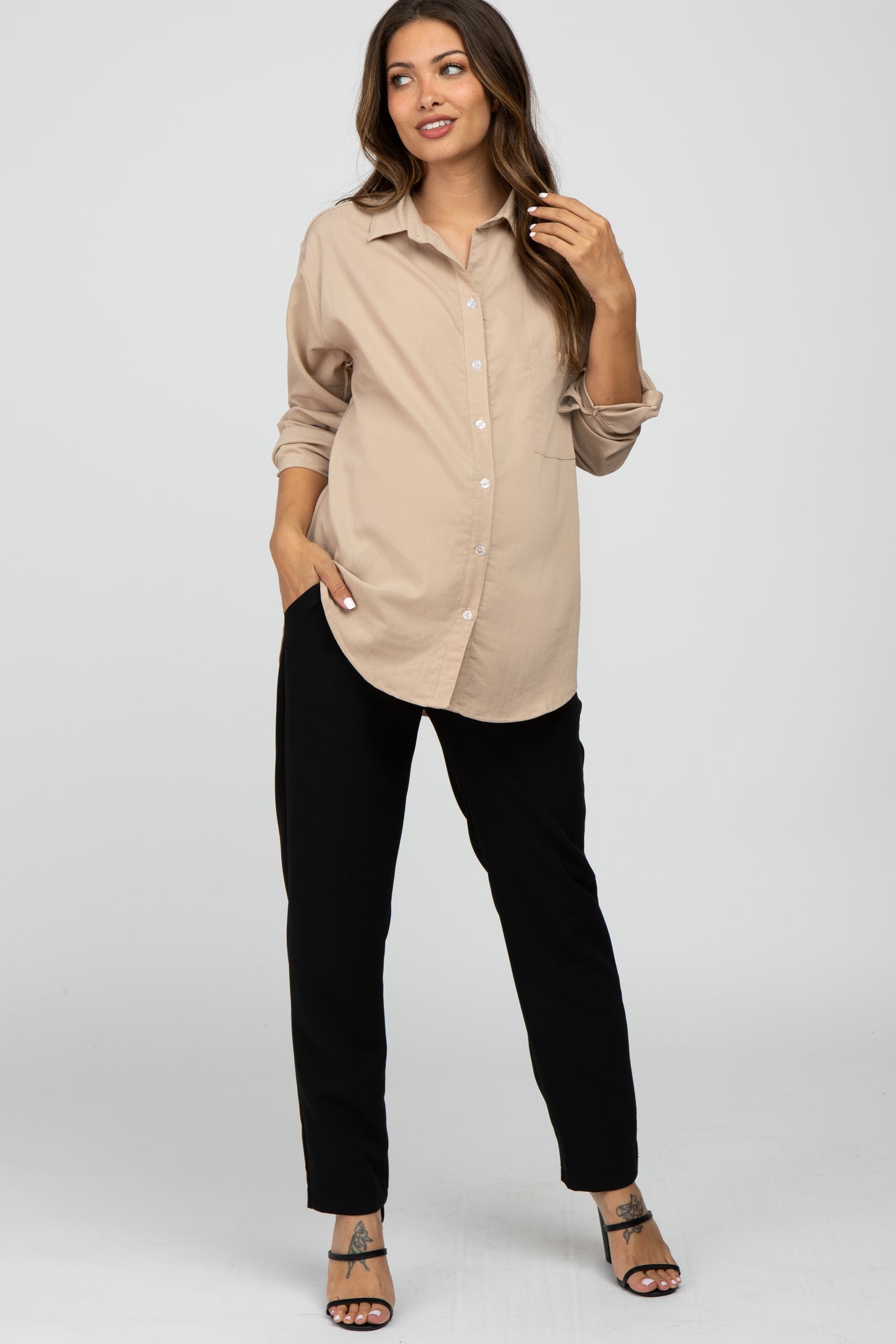 woman wearing a beige button-up maternity shirt and black maternity pants, showing her baby bump