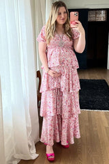 woman wearing a pink floral maternity dress with tiered ruffles and holding her baby bump
