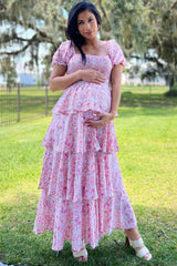 woman wearing a pink floral maternity maxi dress with tiered ruffles and holding her baby bump