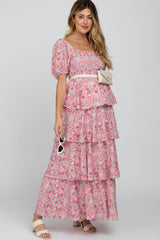 woman wearing a pink floral maternity dress with tiered ruffles and a white belt, styled with sunglasses and a small bag