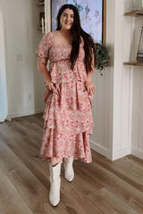 woman wearing a pink floral maternity dress with tiered layers and short sleeves, styled with white boots