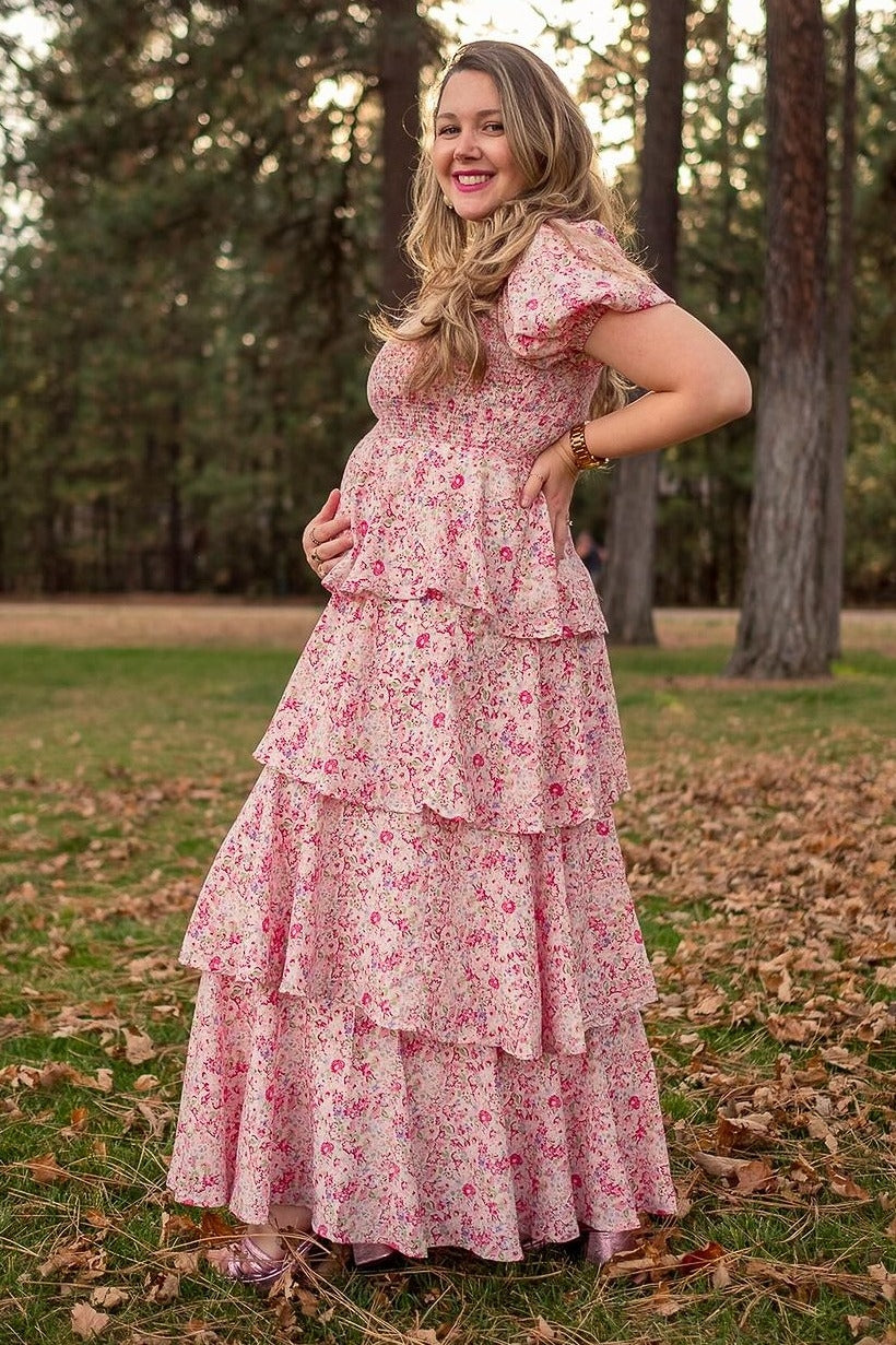 woman wearing a pink floral maternity maxi dress with tiered ruffles and a visible baby bump