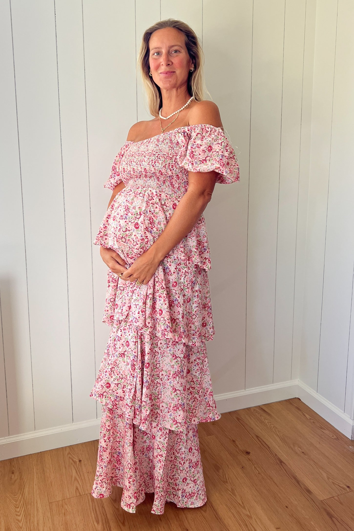 woman wearing a pink floral off-the-shoulder maternity dress with ruffle tiers and holding her baby bump