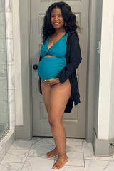 woman wearing a teal maternity swimsuit with a plunging neckline and holding her baby bump in a bathroom setting