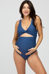 woman wearing a navy blue maternity swimsuit with a cutout detail and holding her baby bump