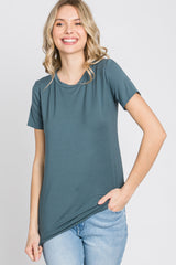 woman wearing a dark teal short sleeve t-shirt paired with light blue jeans and smiling at the camera