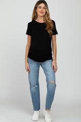 woman wearing a black short sleeve maternity top and distressed light blue jeans, displaying a baby bump
