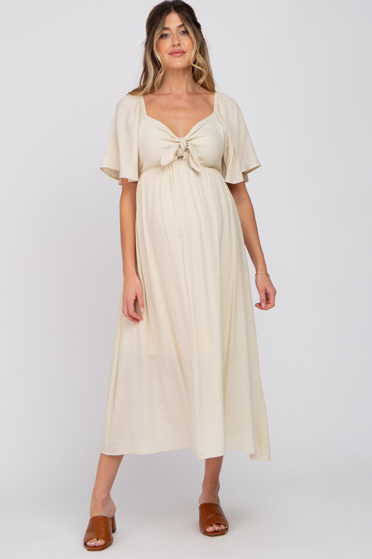 woman wearing a cream maternity dress with short flutter sleeves and a knotted front detail, showing her baby bump