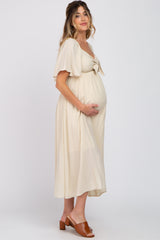 woman wearing a cream maternity dress with short flutter sleeves and a tie front, holding her baby bump