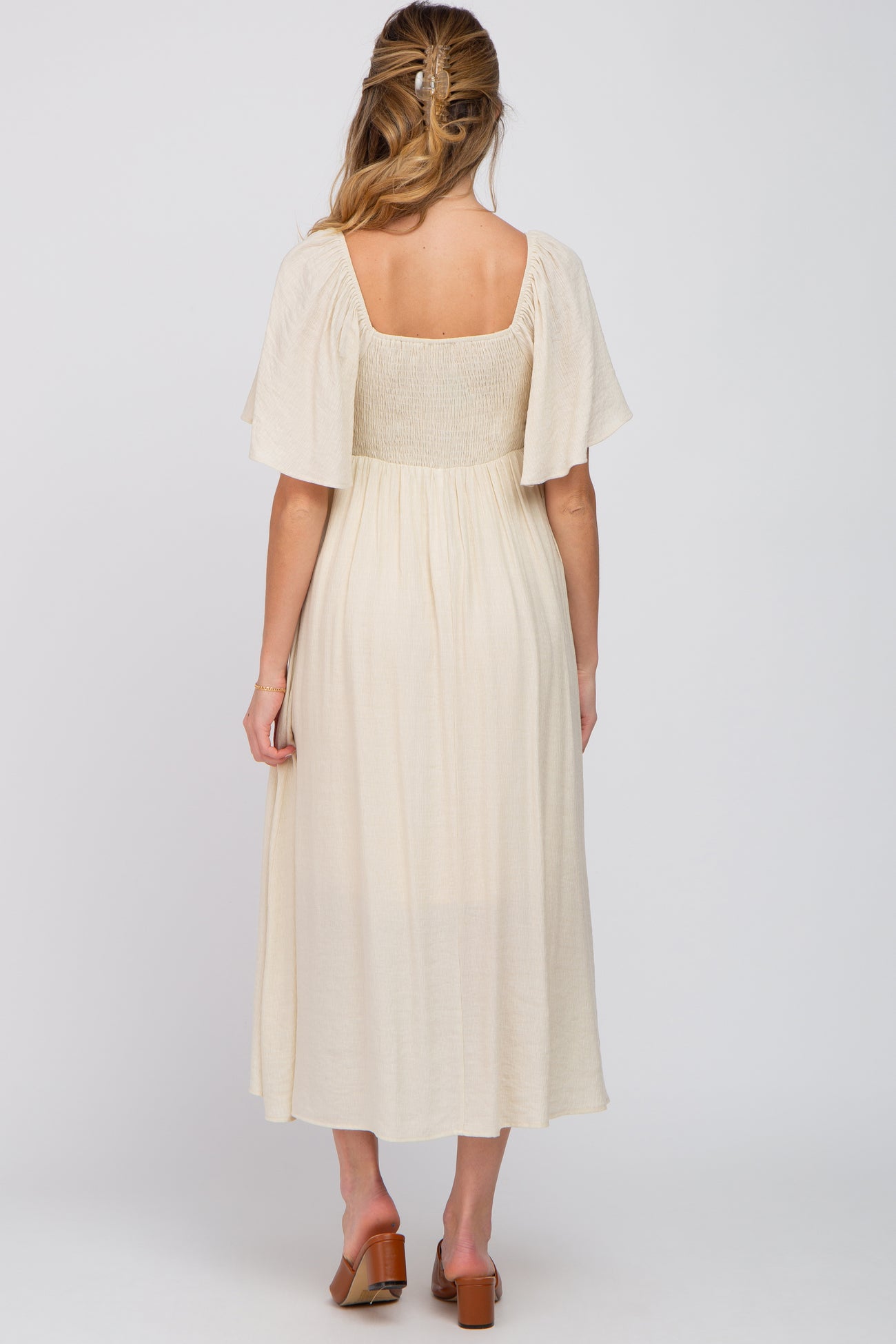 woman wearing a cream-colored maternity dress with flutter sleeves and a smocked bodice, showing a visible baby bump from behind