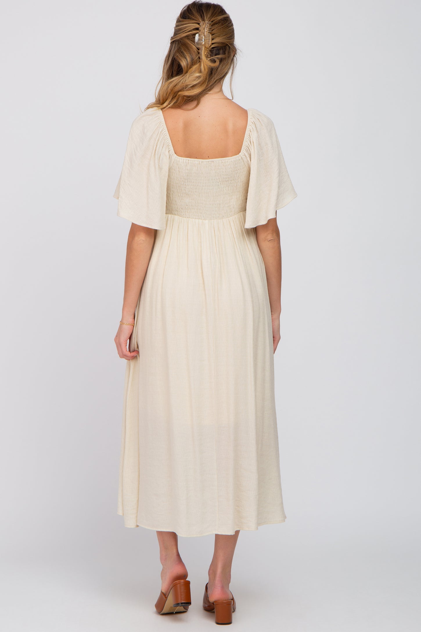 woman wearing a cream-colored maternity dress with flutter sleeves and a smocked bodice, showing a visible baby bump from behind