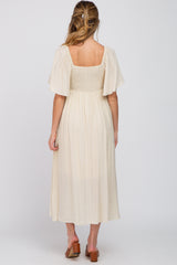 woman wearing a cream-colored maternity dress with flutter sleeves and a smocked bodice, showing a visible baby bump from behind
