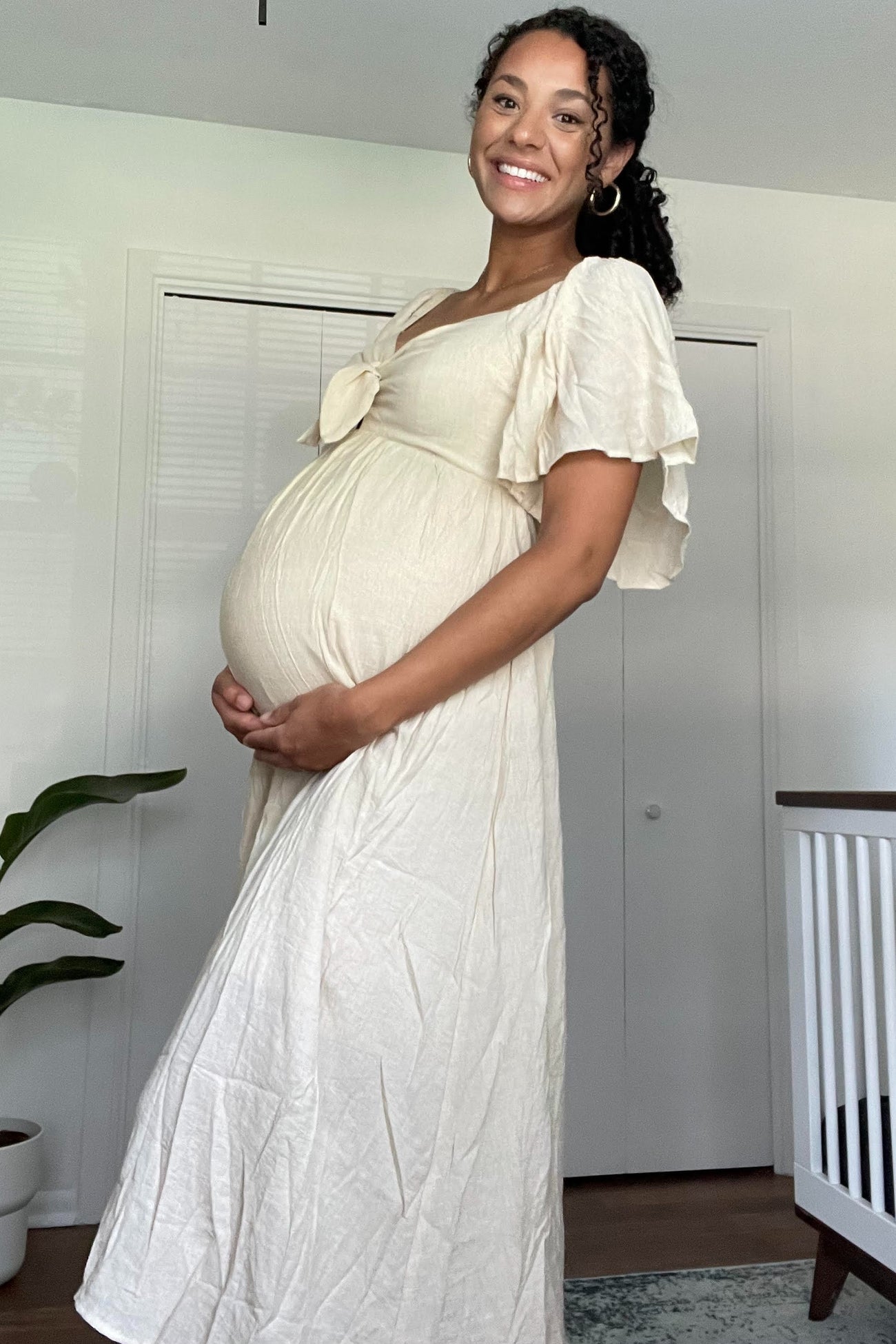woman wearing a cream-colored maternity dress with flutter sleeves and cradling her baby bump