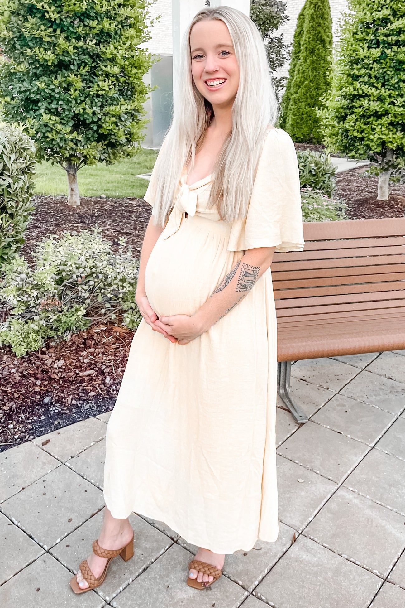 woman wearing a beige maternity maxi dress with a tie front, showing her baby bump while smiling outdoors