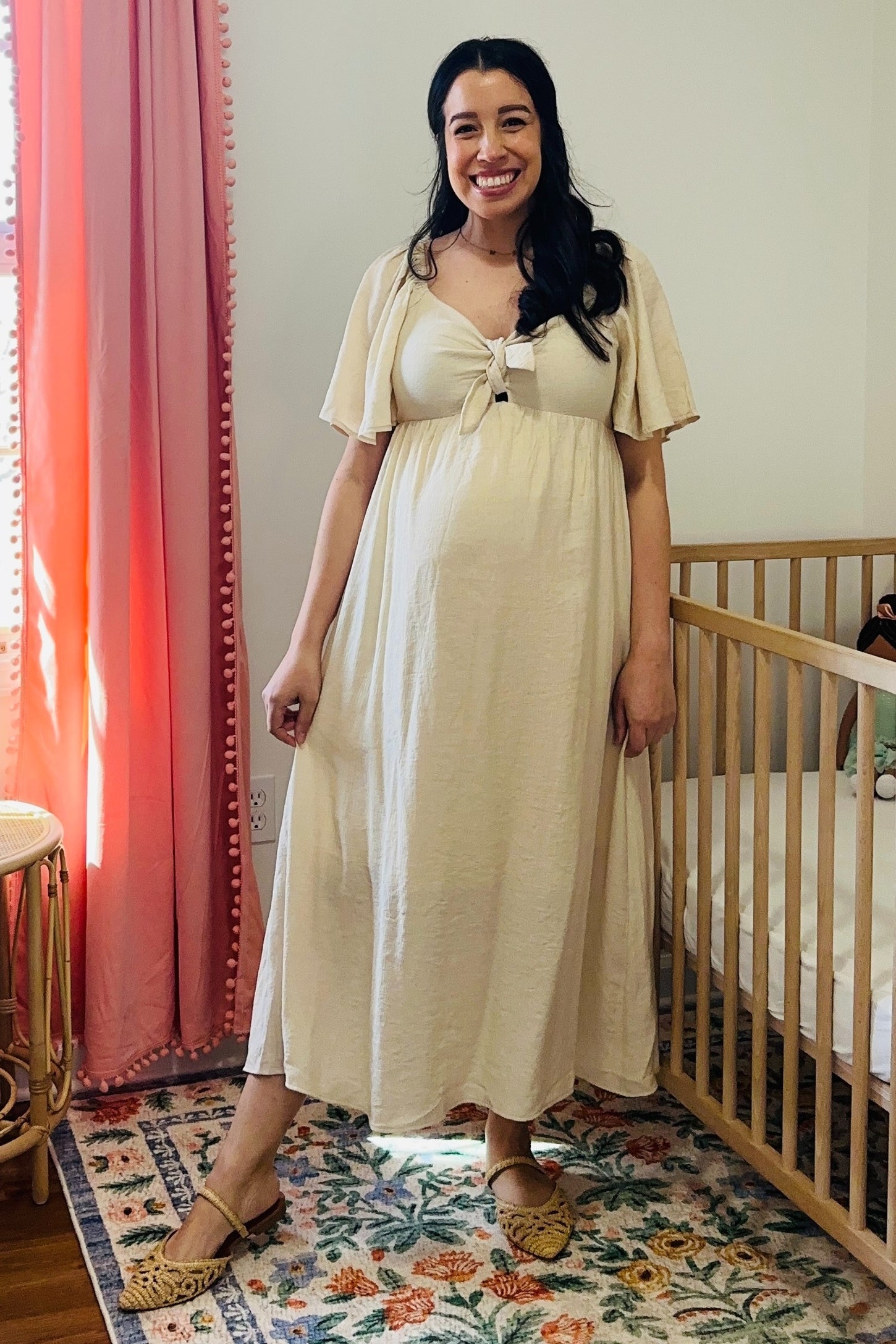 woman wearing a light beige maternity maxi dress with a tie-front detail and short sleeves, standing with a baby bump