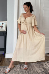 woman wearing a cream maternity dress with a tie-front detail and short sleeves, highlighting her baby bump