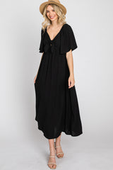 woman wearing a black maxi dress with a tie front and flutter sleeves, accessorized with a straw hat and strappy sandals