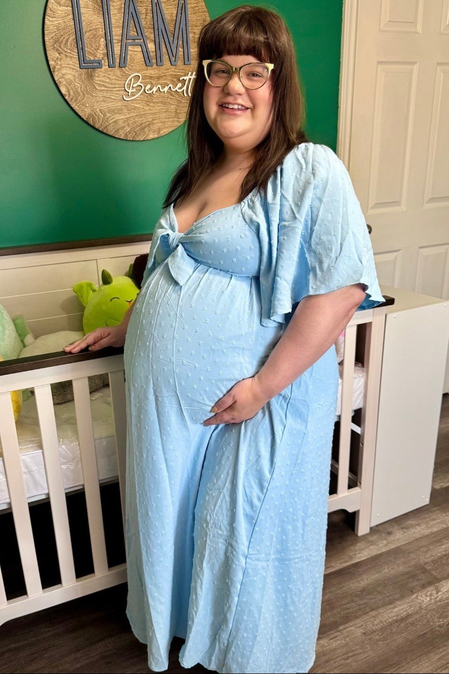 woman wearing a light blue maternity dress with polka dots and short sleeves, showing her baby bump