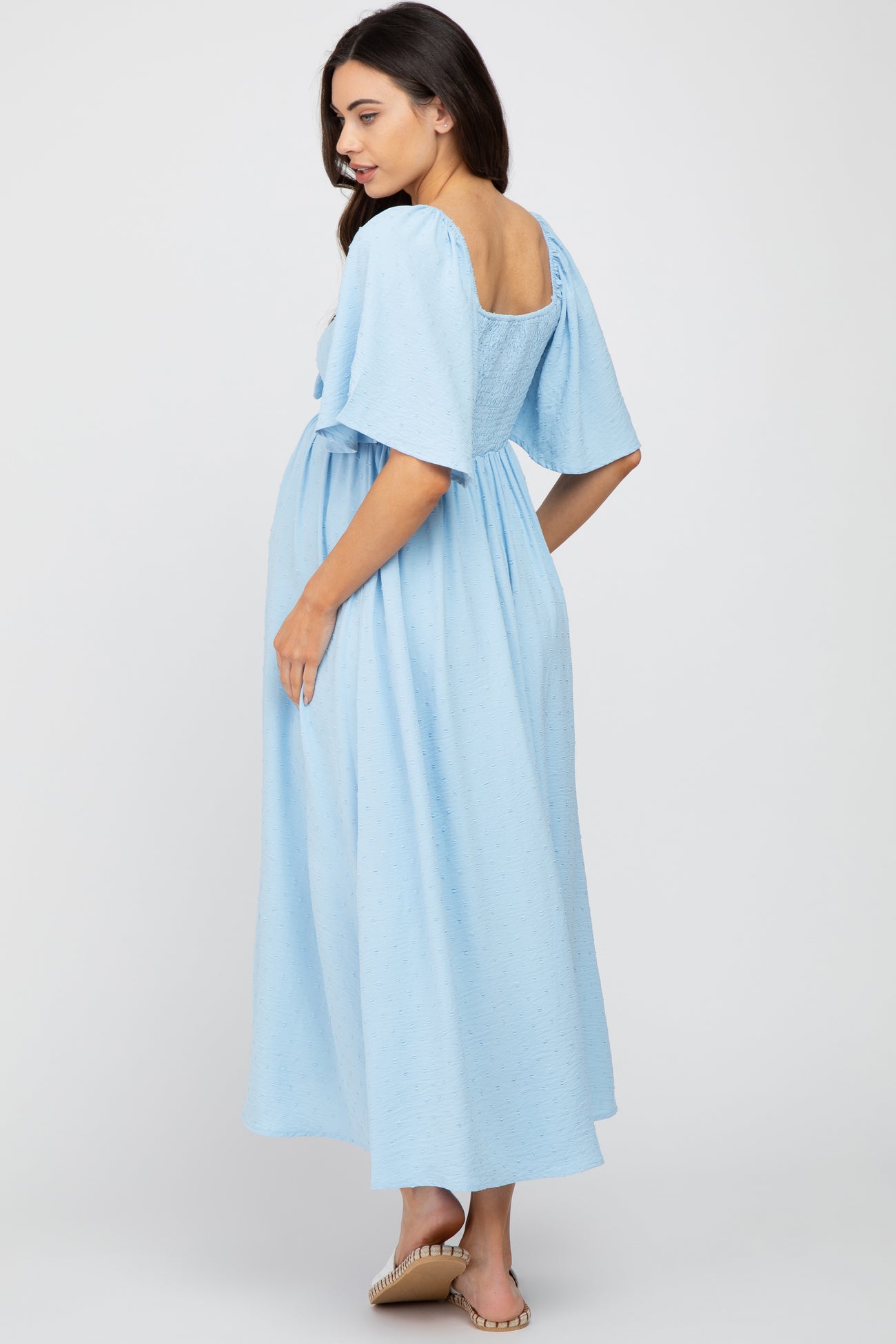 woman wearing a light blue maternity dress with short puff sleeves and a loose fit, showing her baby bump from the back