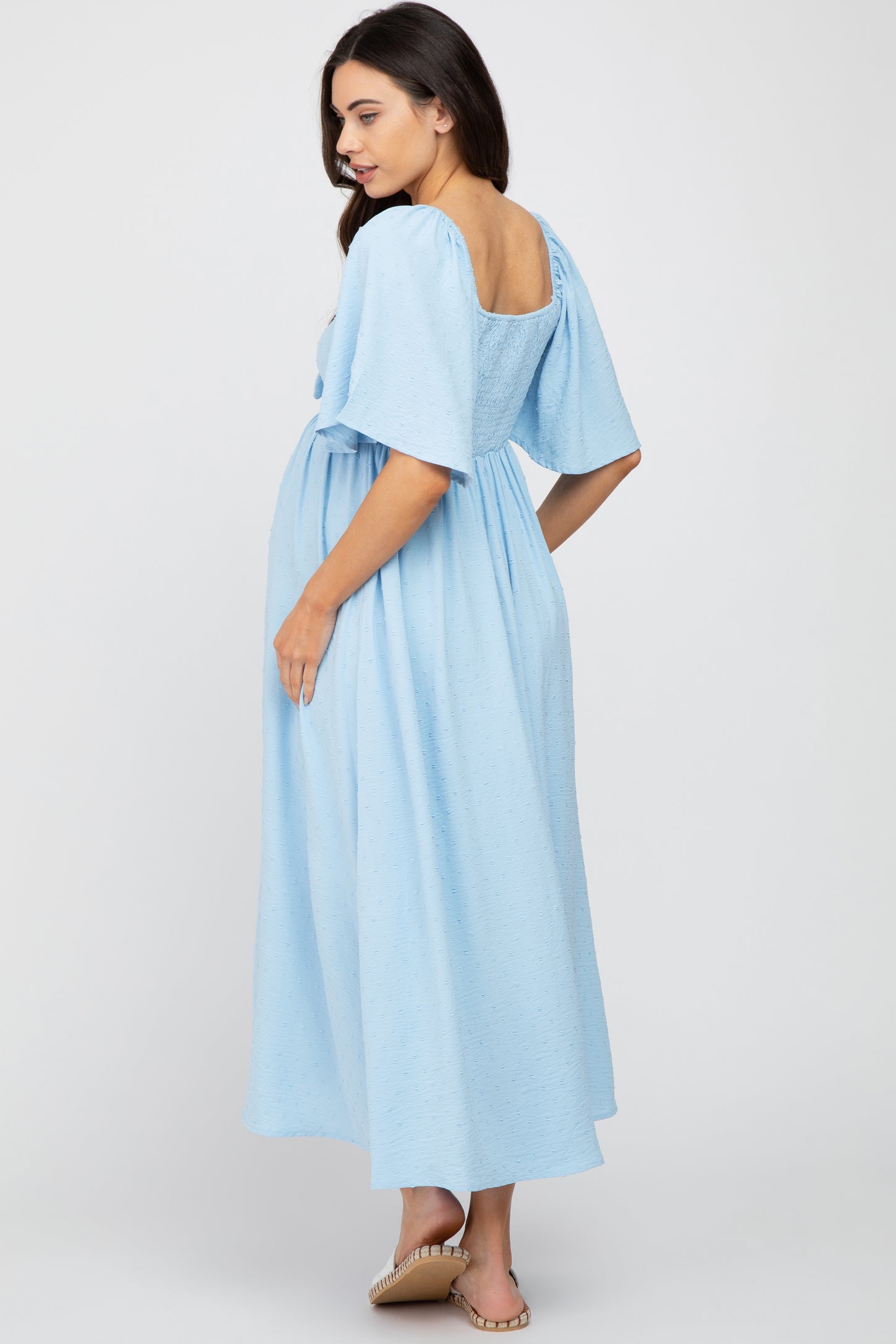 woman wearing a light blue maternity dress with short puff sleeves and a loose fit, showing her baby bump from the back