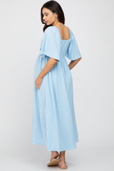 woman wearing a light blue maternity dress with short puff sleeves and a loose fit, showing her baby bump from the back