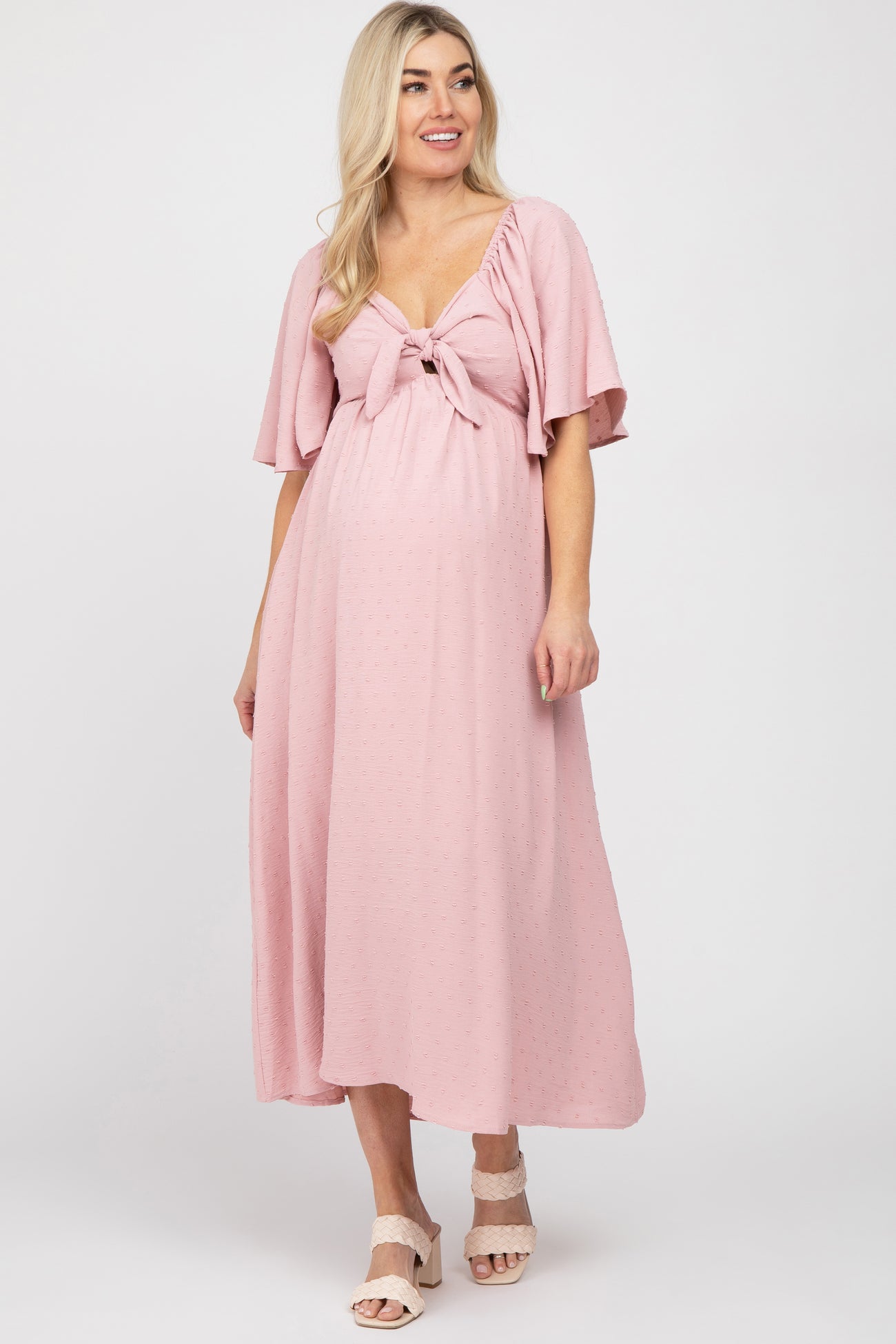woman wearing a light pink maternity dress with a tie front and flutter sleeves, showing her baby bump