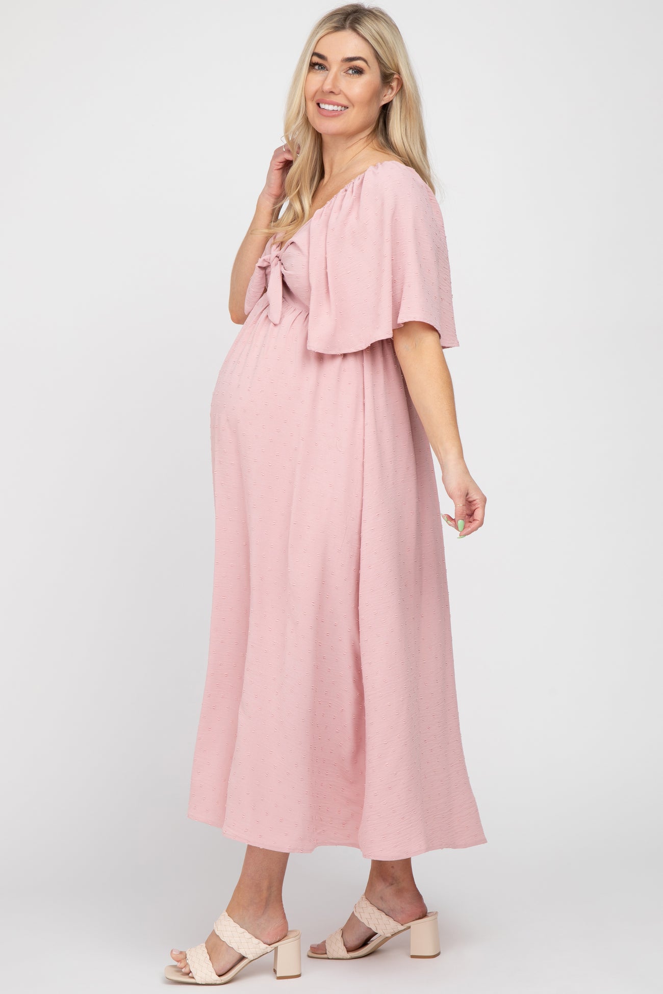 woman wearing a pink maternity dress with a tie-front detail and flutter sleeves, showcasing her baby bump