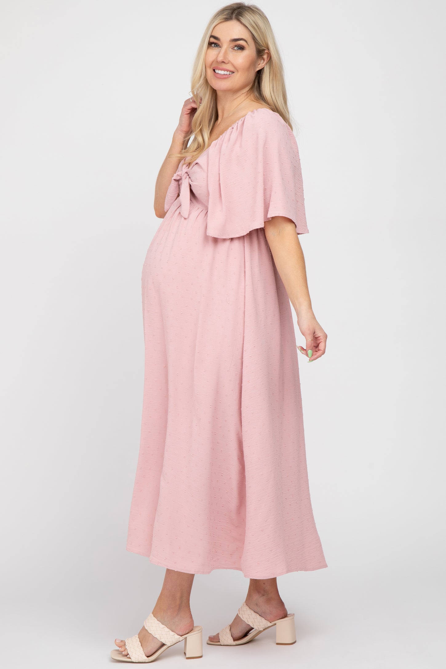 woman wearing a pink maternity dress with a tie-front detail and flutter sleeves, showcasing her baby bump