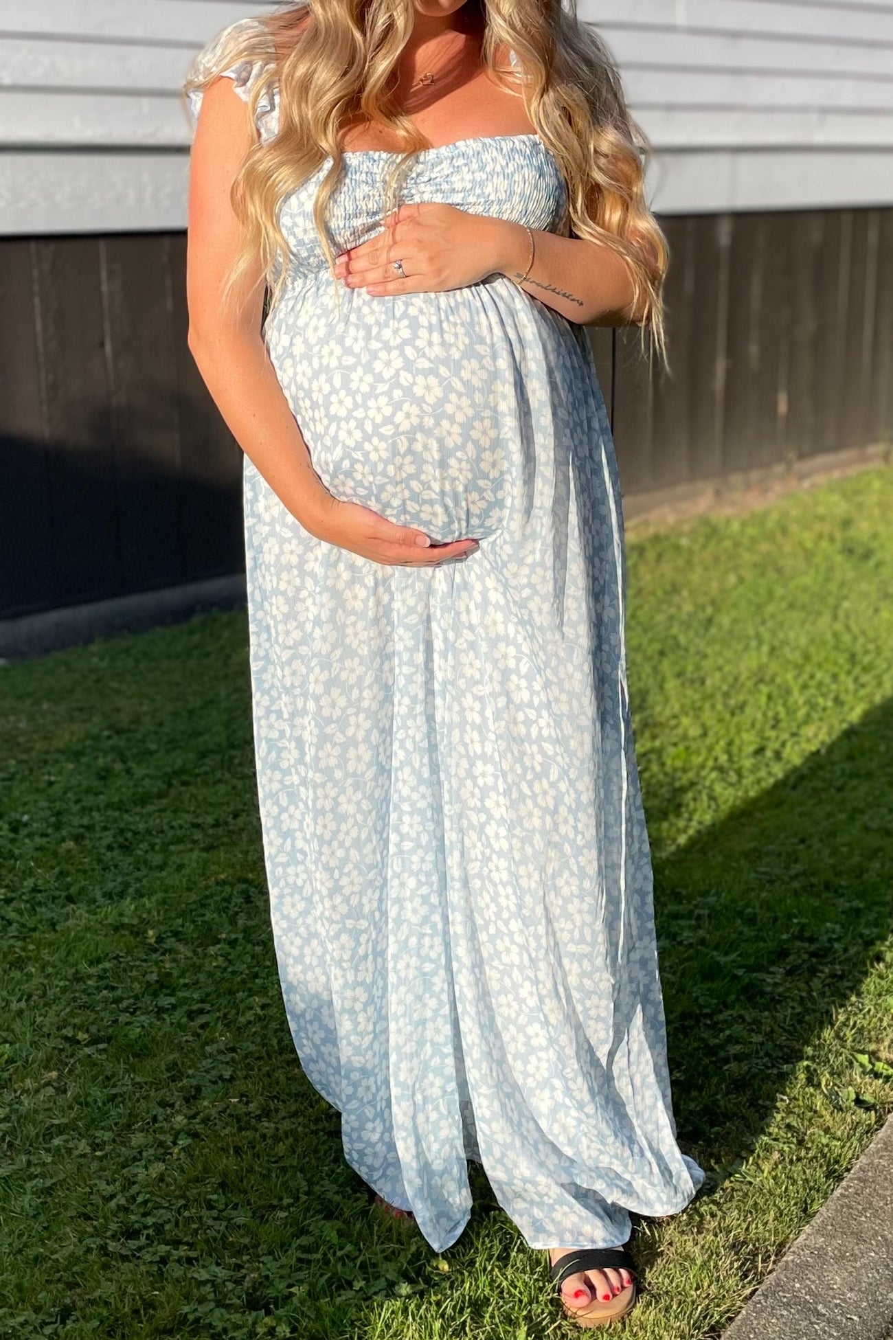 woman wearing a light blue floral maternity maxi dress and holding her baby bump