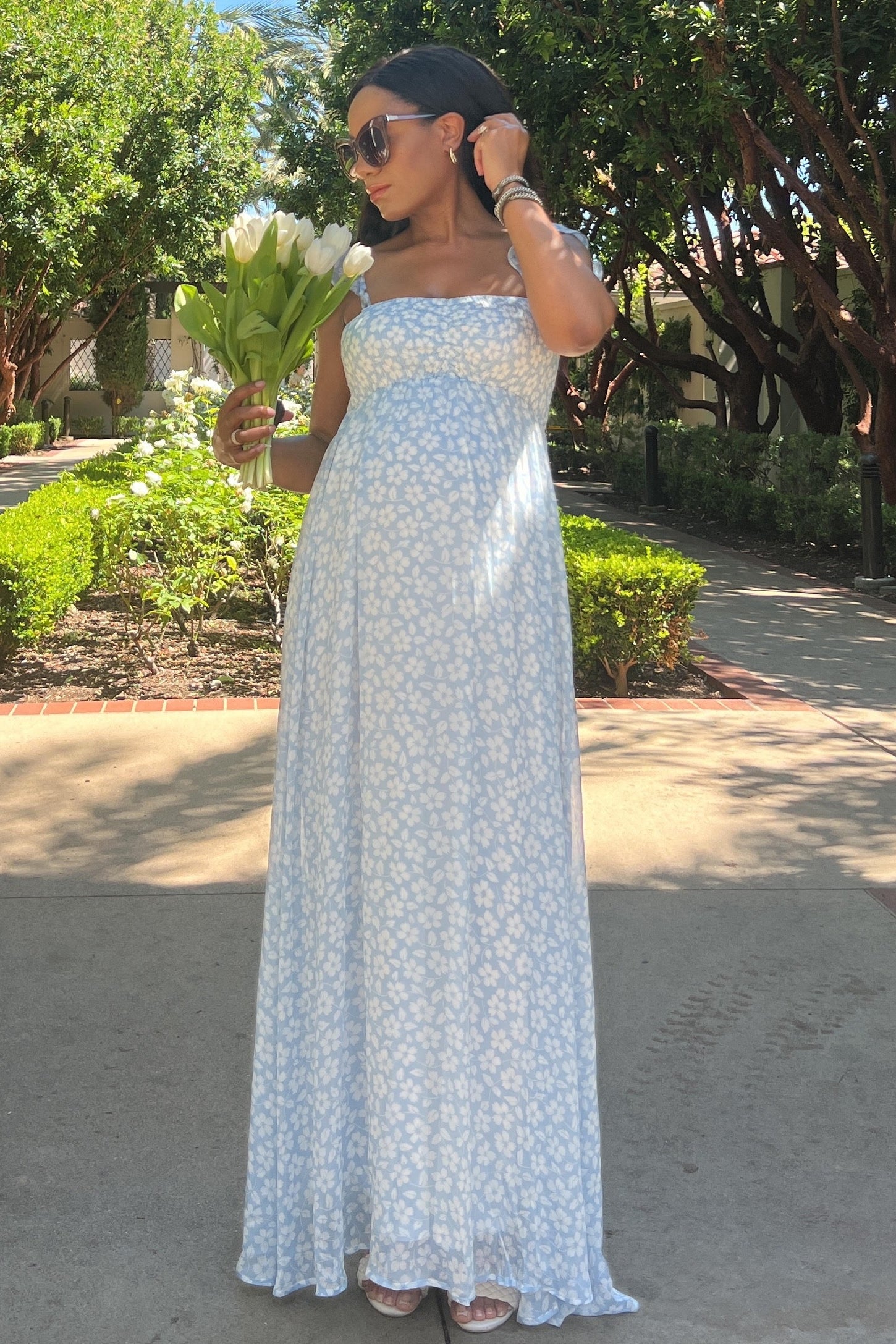 woman wearing a light blue floral maternity maxi dress and holding a bouquet of white tulips with a visible baby bump