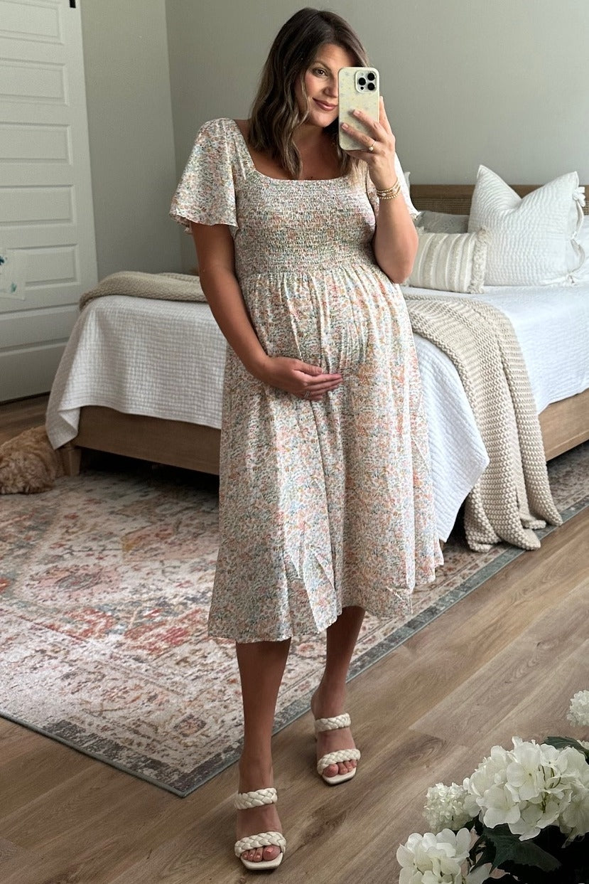 woman wearing a floral print maternity dress with short sleeves and holding her baby bump