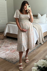 woman wearing a floral print maternity dress with short sleeves and holding her baby bump