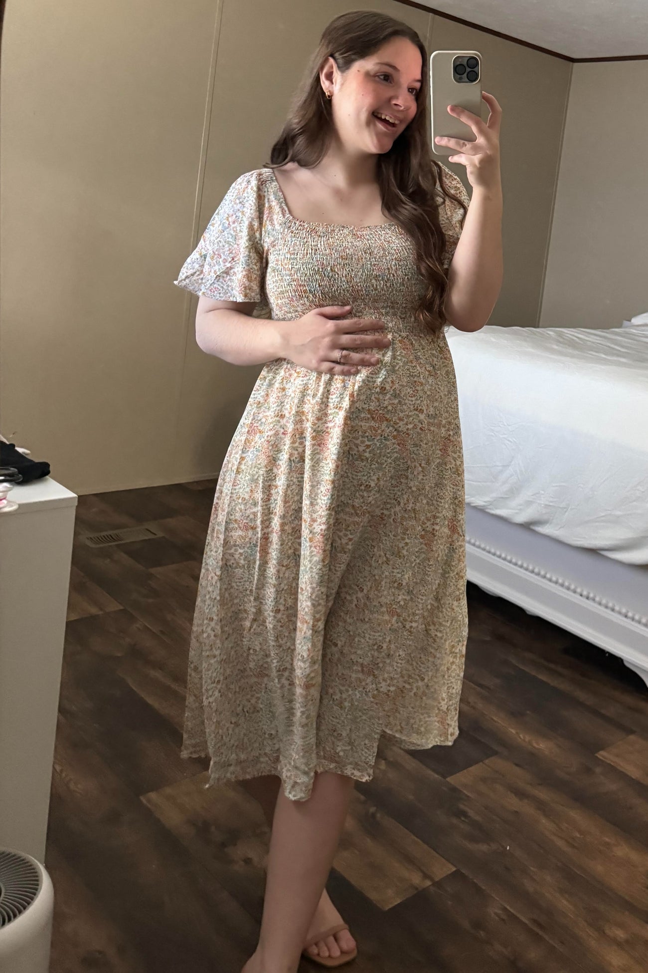 woman wearing a floral print maternity dress with short sleeves and a baby bump, smiling in a mirror selfie