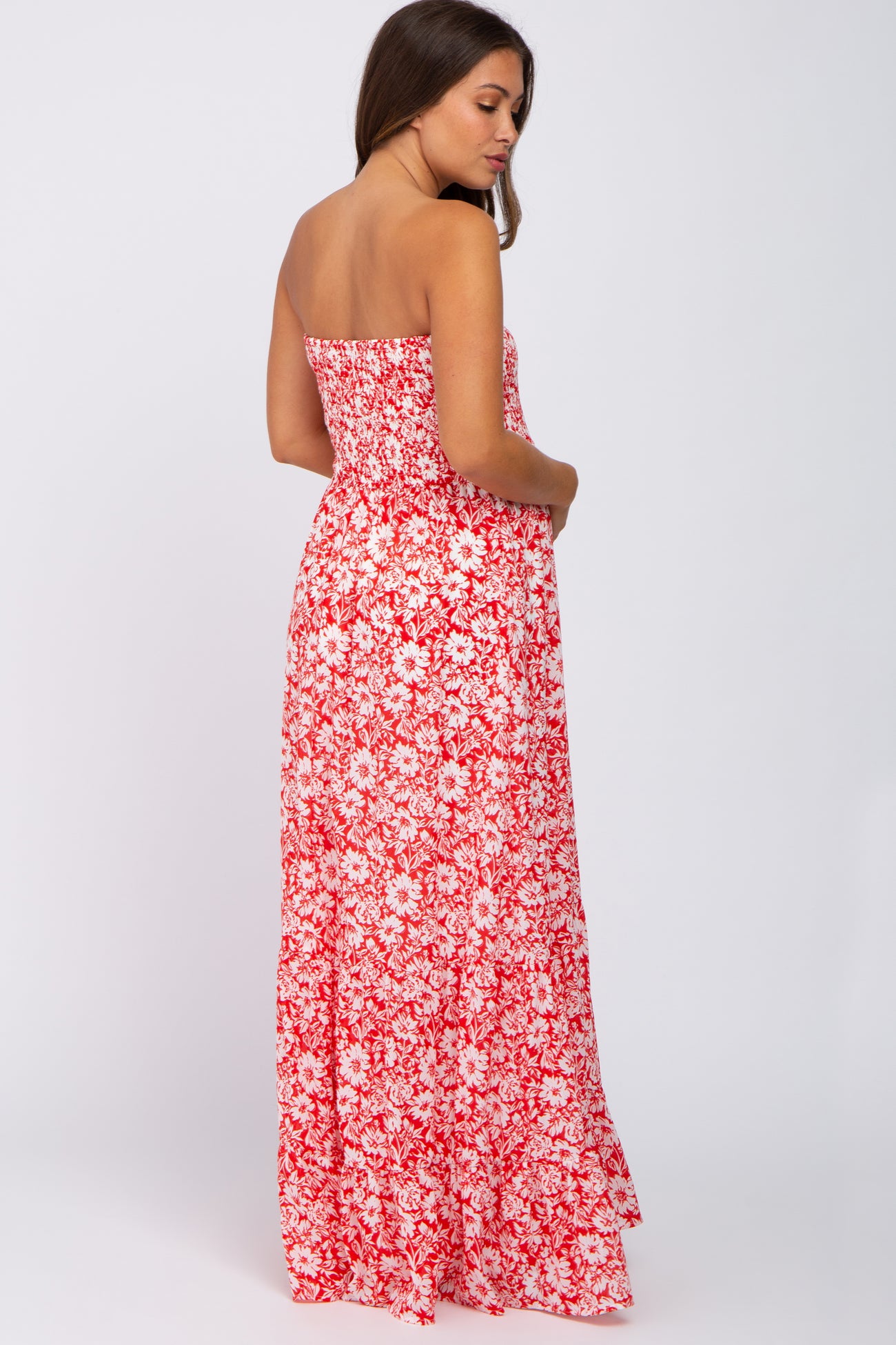 woman wearing a strapless red floral maxi dress, showing a flowing silhouette and fitted bodice, with a visible baby bump