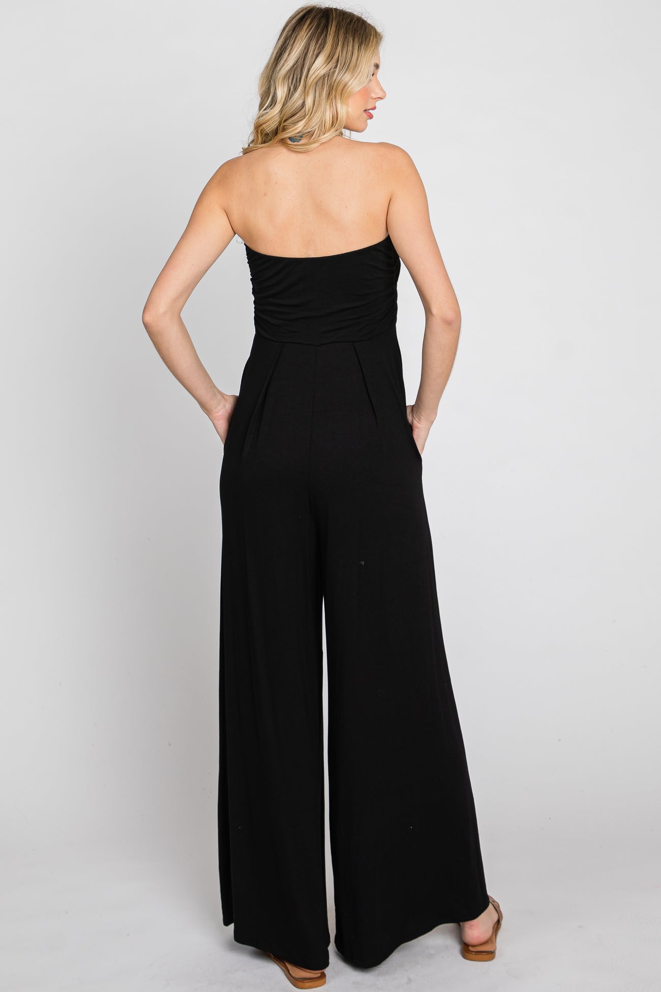 woman wearing a black strapless jumpsuit showcasing a ruched bodice and wide-leg silhouette, viewed from the back