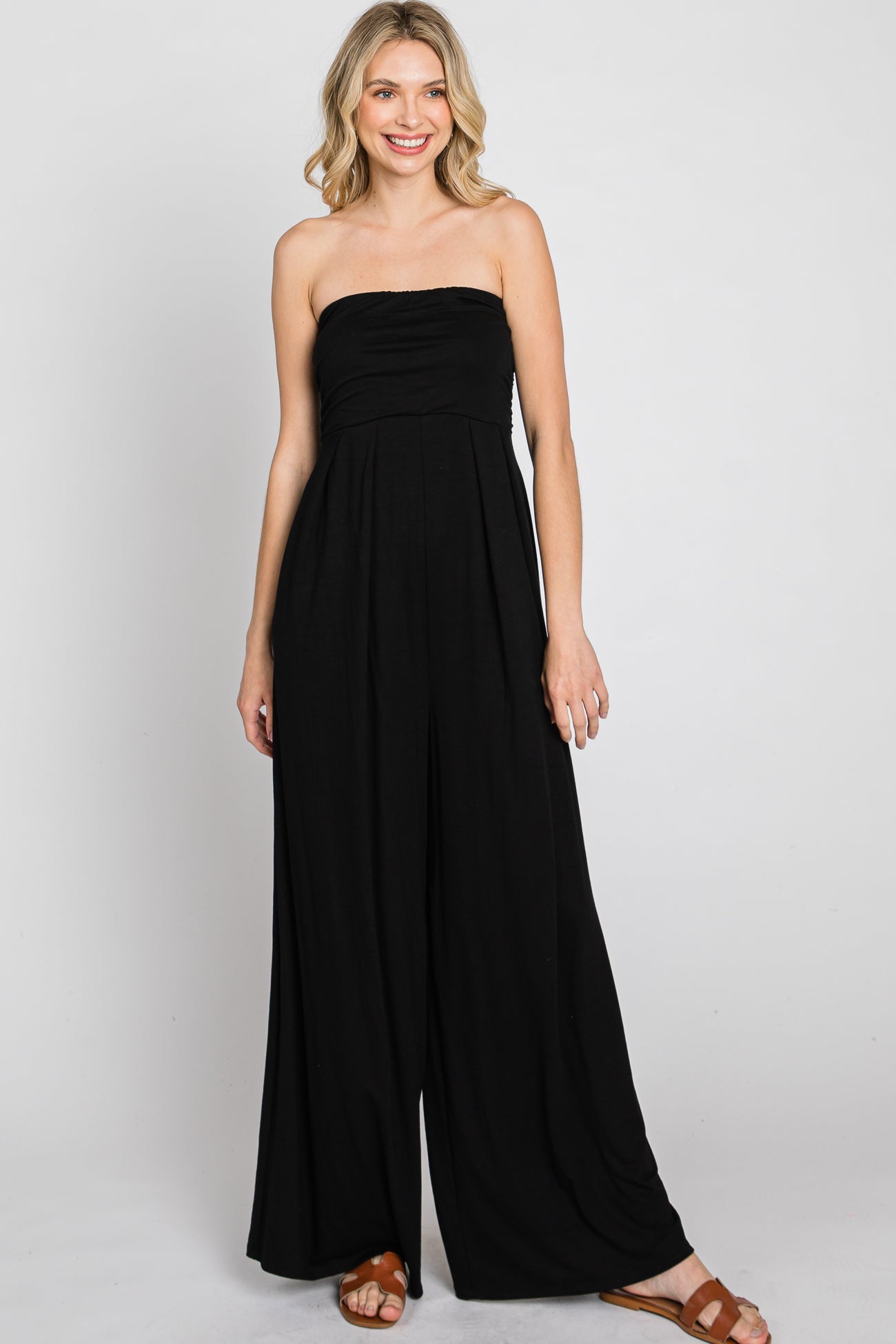 woman wearing a black strapless jumpsuit with a flowing design and wide legs, standing and smiling