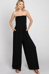 woman wearing a fitted black strapless jumpsuit with pockets and wide legs, standing with hands in pockets