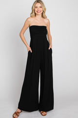 woman wearing a black strapless wide leg jumpsuit with pockets and brown sandals