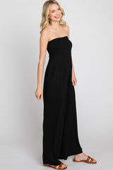 woman wearing a black strapless jumpsuit with a ruched bodice and wide legs, styled with brown sandals