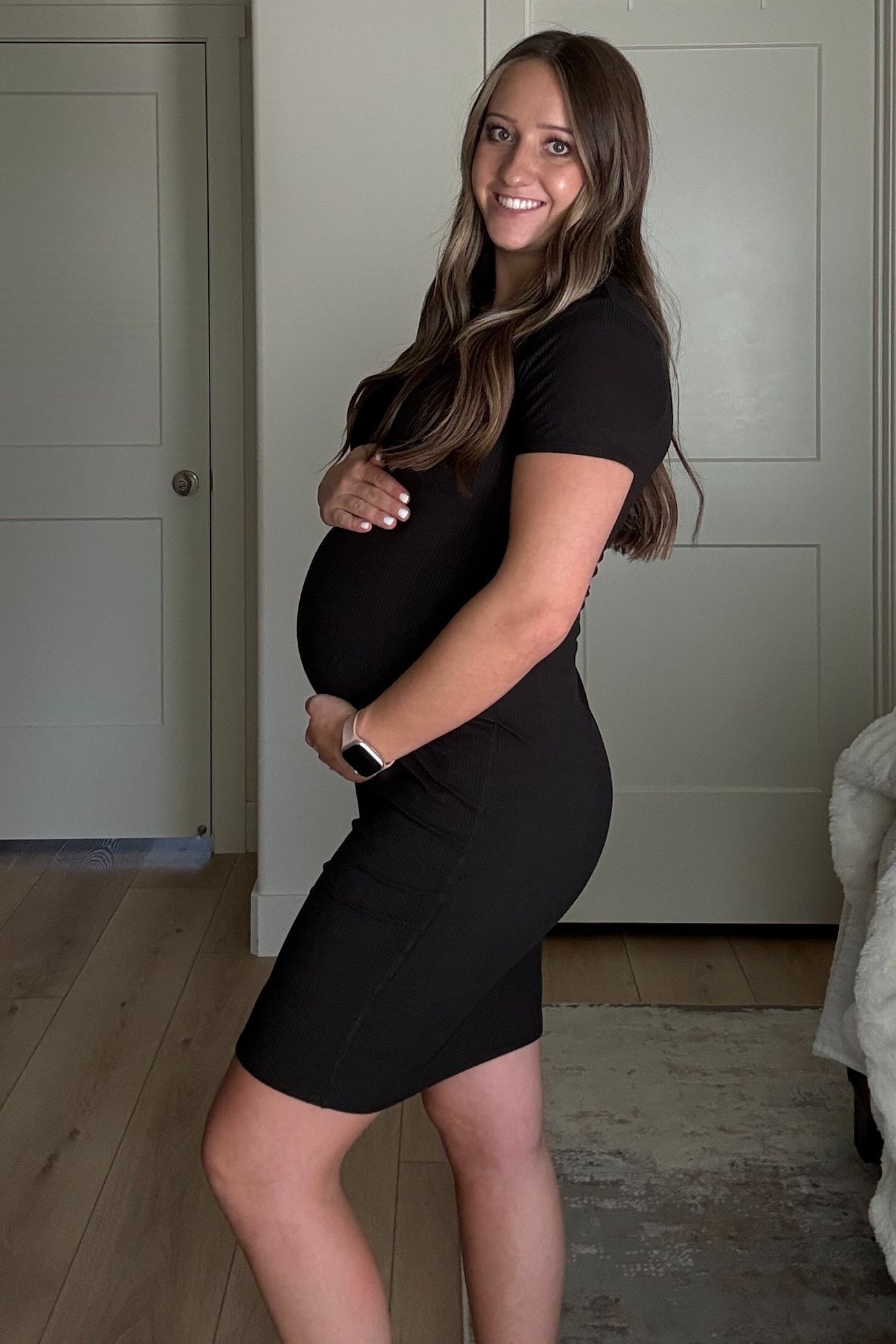 woman wearing a fitted black maternity dress and cradling her baby bump