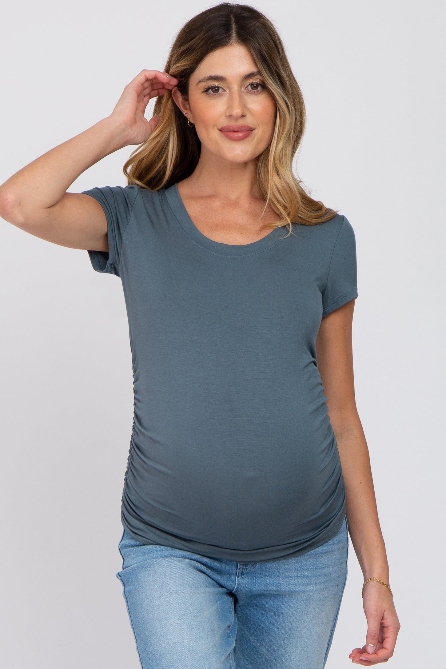 woman wearing a blue short sleeve maternity top, showcasing her baby bump, paired with light blue jeans