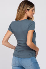 Back view of a woman wearing a fitted slate blue short sleeve maternity top with side ruching and blue jeans