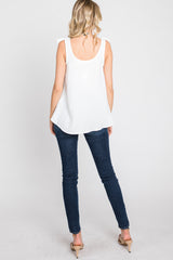 woman wearing a white sleeveless top with ruffle details and dark skinny jeans, viewed from the back