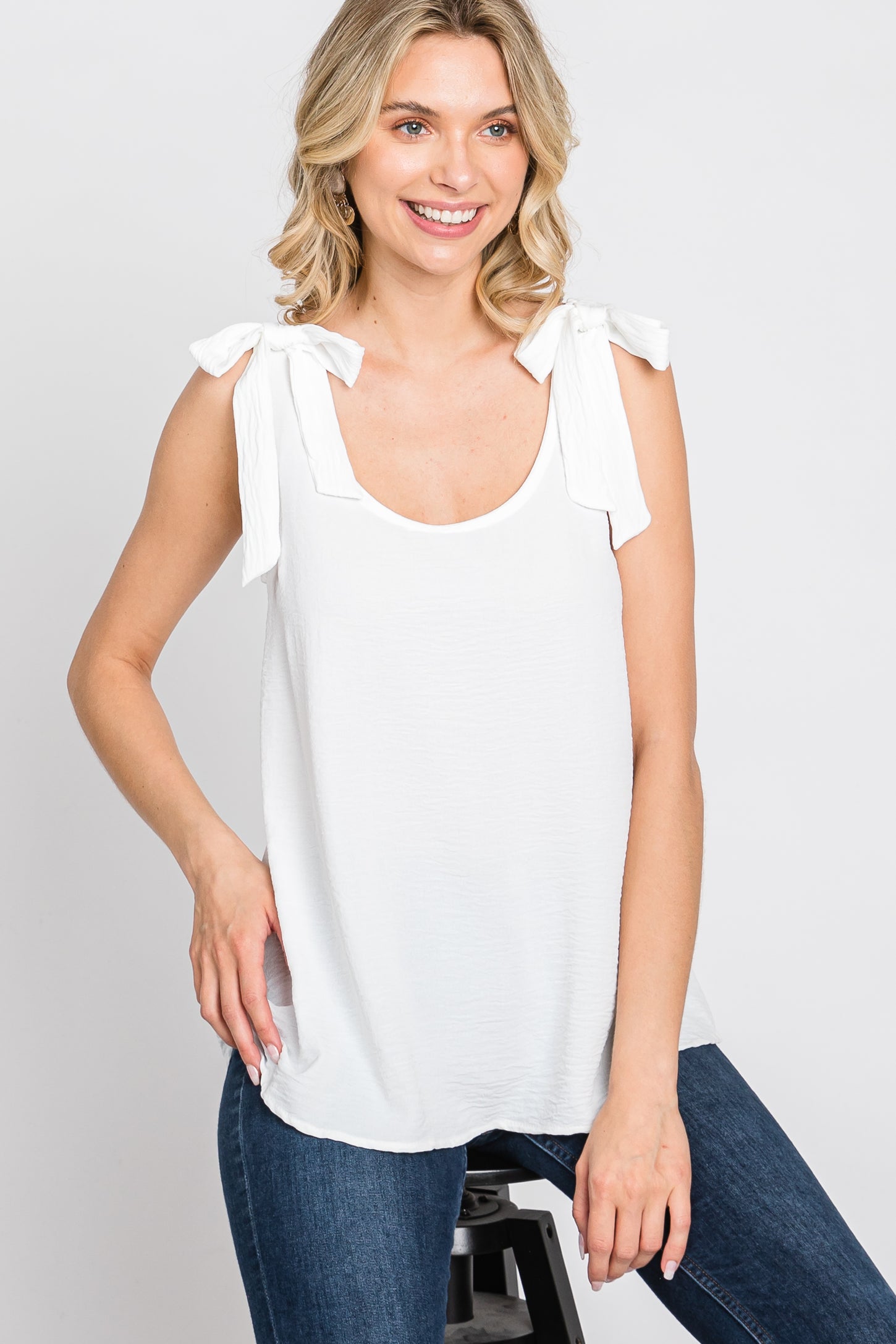 woman wearing a white tank top with tie shoulder details and blue jeans